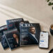 Magazines fanned out on a desk beside a smartphone and coffee cup, styled with warm natural light, representing PR coverage and paid editorial placement.